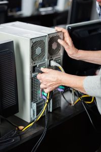 Senior Woman Plugging Computer In Classroom